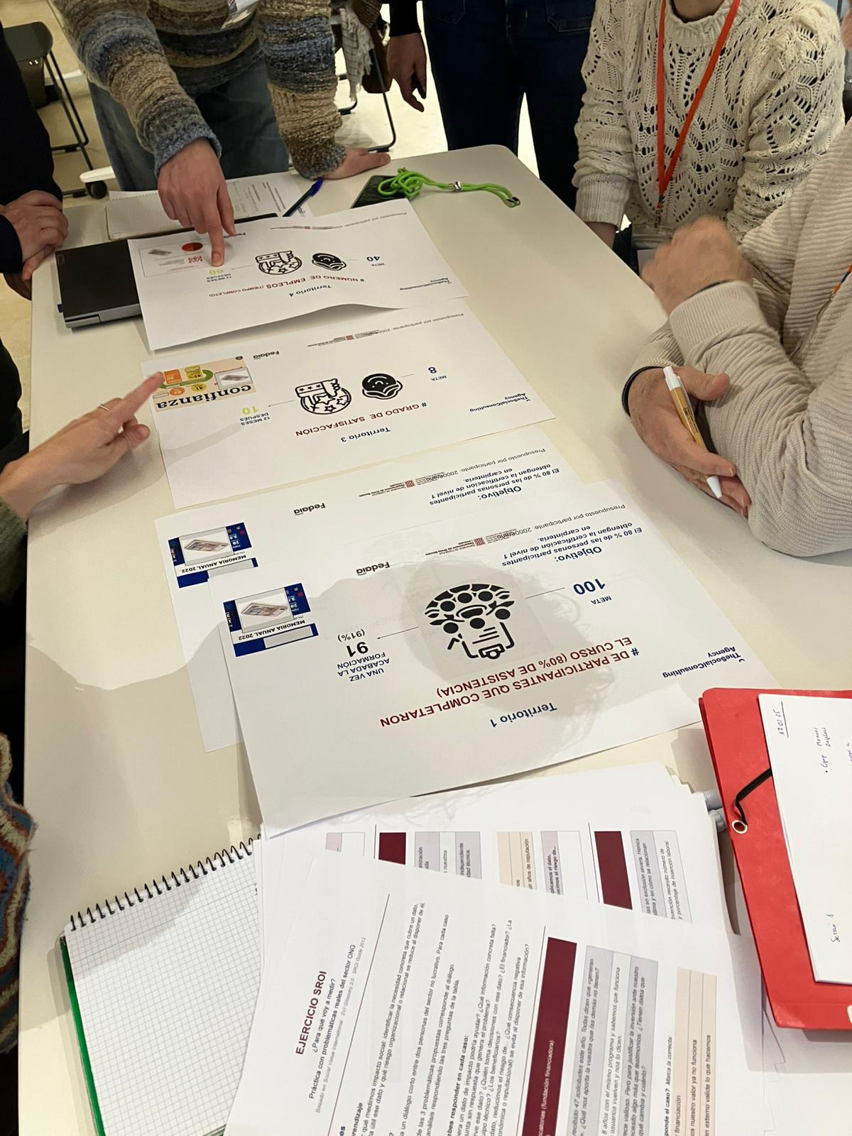 Participantes revisando documentos en una mesa de trabajo durante una formacion de impacto social