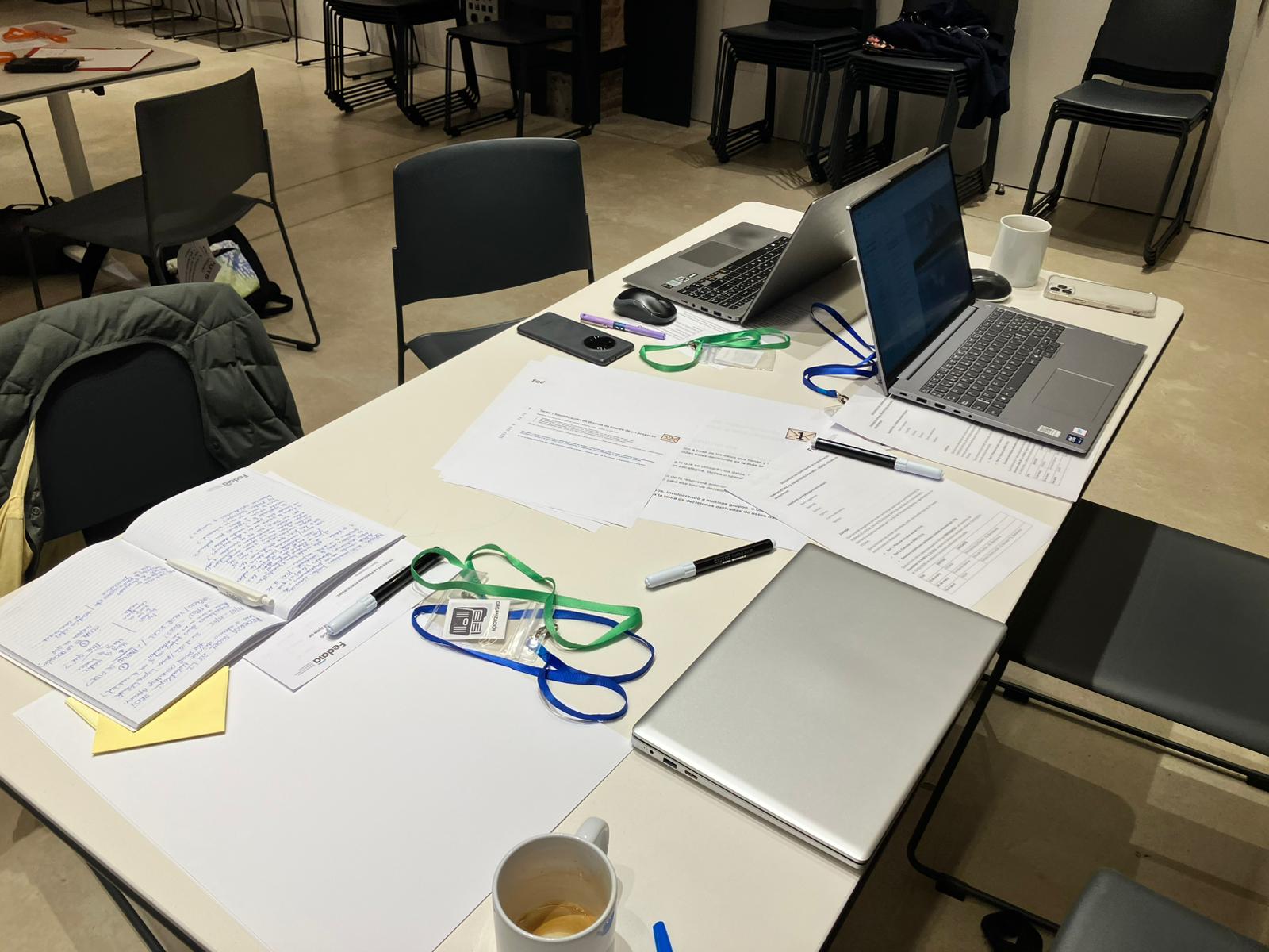 Mesa preparada con portatiles, cuadernos y documentos antes de un taller de medicion de impacto social